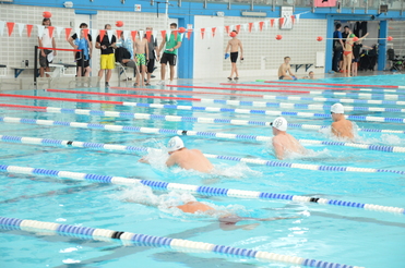 Vier Schwimmer in weißen Badekappen schwimmen in einem Sportbecken mit mehreren Bahnmarkierungen.