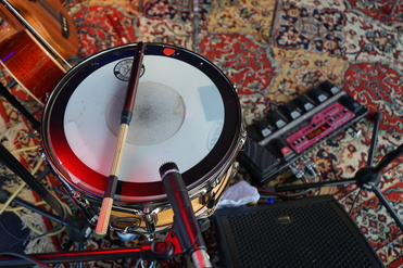 Nahaufnahme einer Snare-Drum mit zwei Sticks, Mikrofon und Effektgerät auf einem bunten Teppich.
