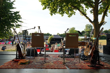 Blick von der Bühne auf leere Stühle und Instrumente vor Publikum auf einer Freiluftveranstaltung.