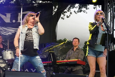 Zwei Sänger auf einer Bühne, ein Mann mit Mikrofon und eine Frau mit Notenständer, im Hintergrund ein Keyboarder.