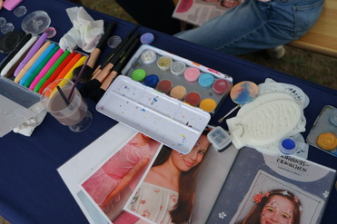 Buntes Make-up-Set mit Pinsel, Paletten und Bildern von geschminkten Kindern auf einem Tisch.