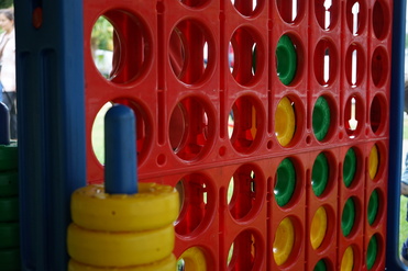 Nahaufnahme eines bunten Vier-gewinnt-Spiels mit roten, gelben und grünen Spielscheiben auf einer Wiese.