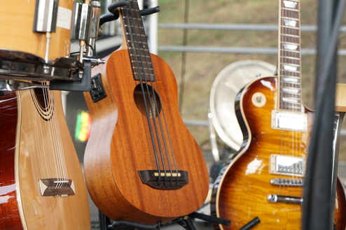 Nahaufnahme von verschiedenen Musikinstrumenten: Ukulele, Akustikgitarre und E-Gitarre auf einer Bühne.