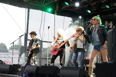 Rockband tritt auf Bühne auf, Musiker mit Instrumenten und Bühnenbeleuchtung, lockere Atmosphäre während des Auftritts.