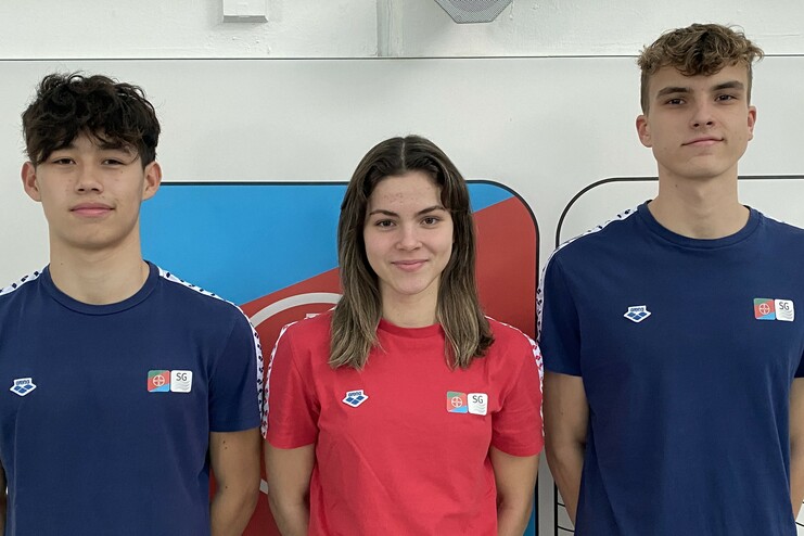 Drei Sportler stehen in Sportbekleidung vor einer bunten Wand, zwei in blauen, einer in rotem Shirt.