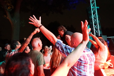 Menschenmenge bei Konzert, Arme in die Luft gehoben, intensives Nachtszenario mit bunten Lichtern.