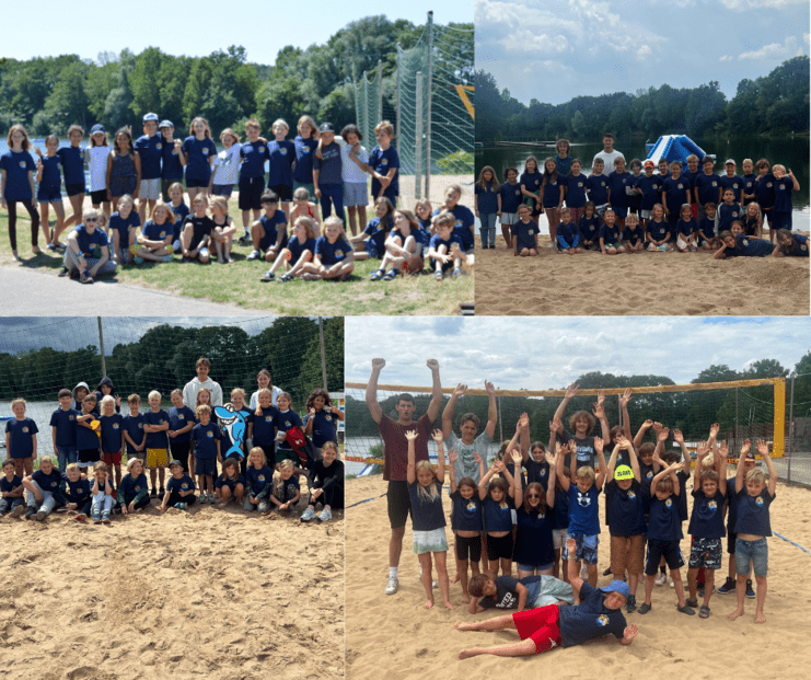 Gruppenfoto von Kindern in blauen T-Shirts am Strand, mit Spielgeräten und Bäumen im Hintergrund.