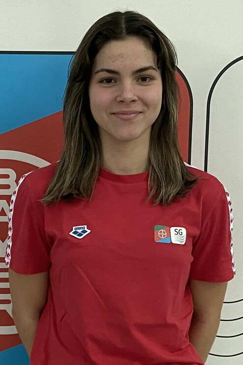 Junge Sportlerin mit langen Haaren und rotem T-Shirt steht vor einem bunten Hintergrund.