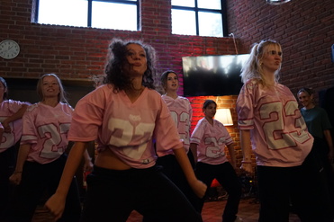Tanzgruppe in pinken Trikots führt eine Choreografie in einem stilvollen Raum mit Backsteinmauer auf.