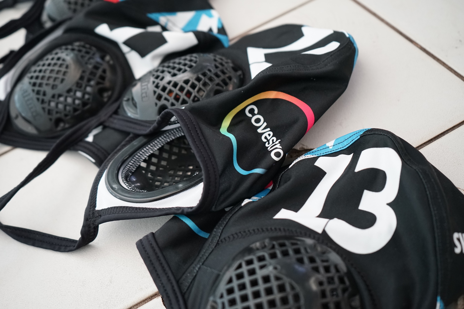 Detailaufnahme von zwei Schutzausrüstungen mit grauen Schutzgittern und dem Aufdruck "Covestro" auf schwarzem Material.