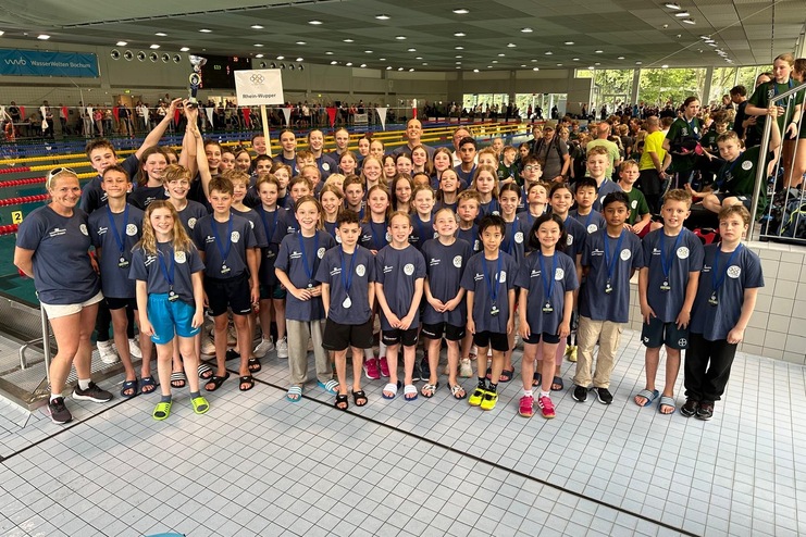 Gruppenshooting von jungen Schwimmern mit Medaillen und Pokal in einem Schwimmbad, jubelnd und erfreut.
