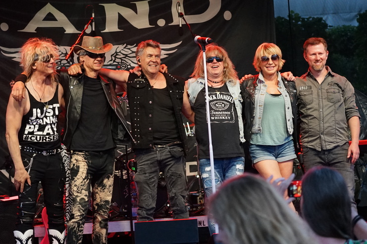 Fünf Musiker posieren lächelnd auf der Bühne vor einem schwarzen Banner mit dem Bandnamen A.N.D.