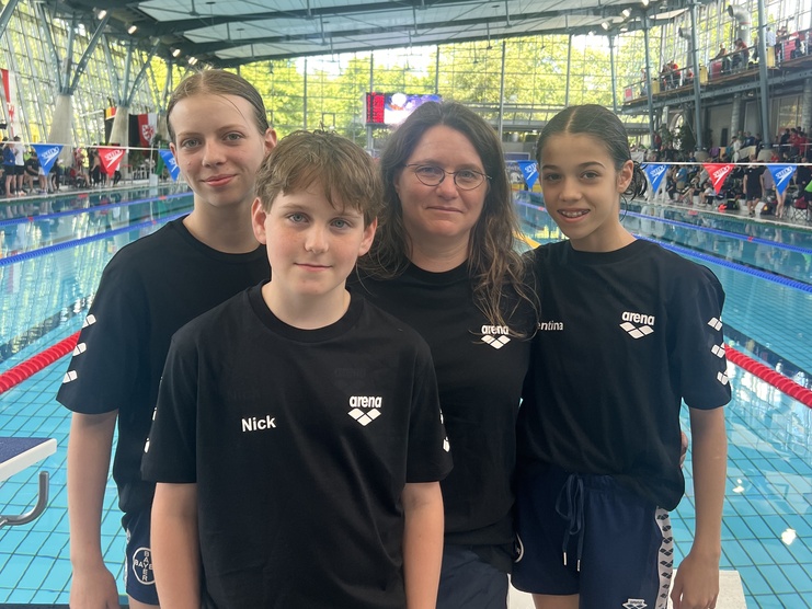 Gruppenbild von vier Schwimmern in schwarzen T-Shirts am Beckenrand eines Schwimmbads.