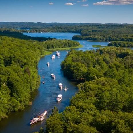 Luftaufnahme eines Flusses, umgeben von Bäumen, mit mehreren Booten auf dem Wasser im Hintergrund.
