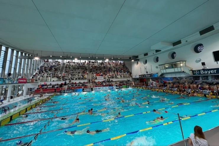 Schwimmveranstaltung in einem Hallenbad mit zahlreichen Schwimmern und Zuschauern auf den Rängen.