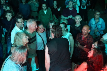 Menschen feiern in einer bunten Menschenmenge, einige stehen näher zusammen und lächeln, umgeben von Lichtern.