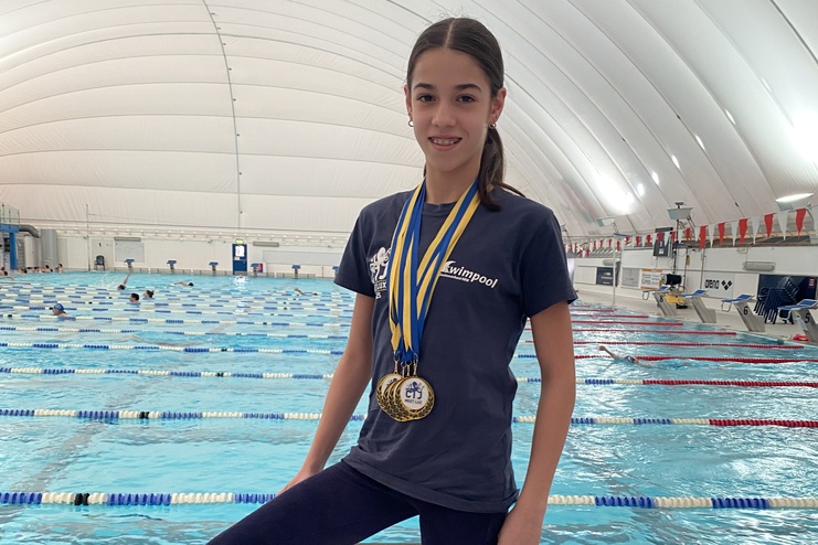 Mädchen mit Medaillen auf einem Startblock in Schwimmhalle, Schwimmbecken im Hintergrund.