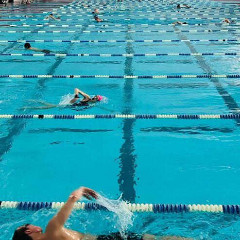 Schwimmer trainiert im Becken eines Hallenbades mit mehreren Schwimmbahnen und geringer Besucheranzahl.