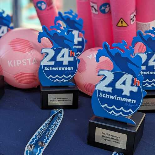 Preise für das 24-Stunden-Schwimmen: Pokale für längste Strecken, pinke Bälle und Ruten auf einem Tisch.