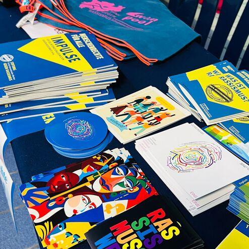 Vielfalt an bunten Informationsmaterialien und Merchandise-Artikeln auf einem Tisch bei einem Schwimmerevent.