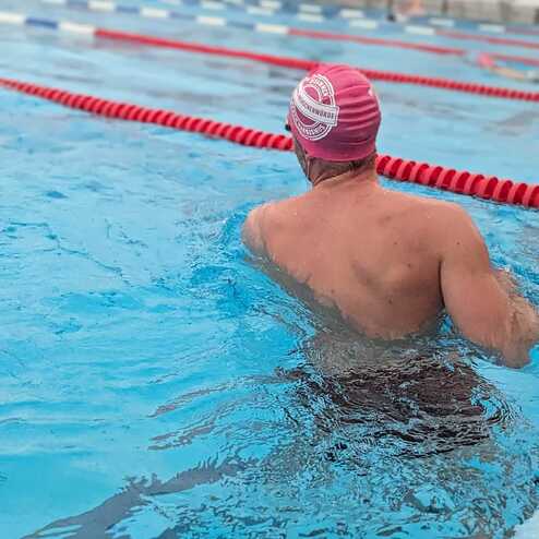 Schwimmer mit rosafarbenem Badekäppchen schwimmt im blauen Wasser eines Schwimmbeckens. Rote Bahnmarkierungen sind sichtbar.
