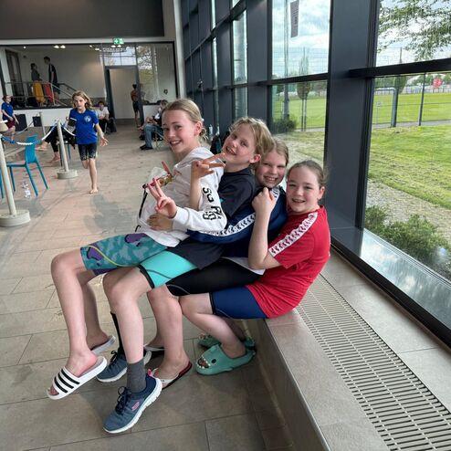 Vier Kinder sitzen fröhlich auf einer Fensterbank, während ein weiteres Kind im Hintergrund vorbeiläuft.