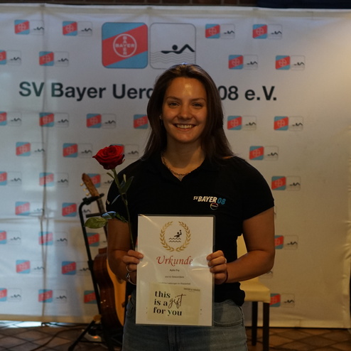 Junge Frau hält eine Urkunde und eine rote Rose, steht vor einem Banner des SV Bayer Uerdingen 08 e.V.