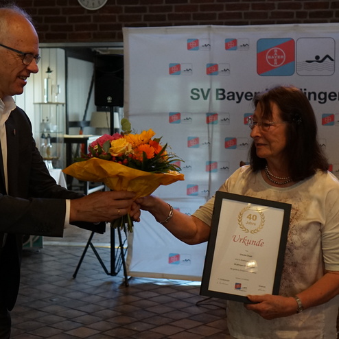 Ein Mann überreicht einer Frau einen Blumenstrauß und eine Urkunde zum 40-jährigen Vereinsjubiläum.