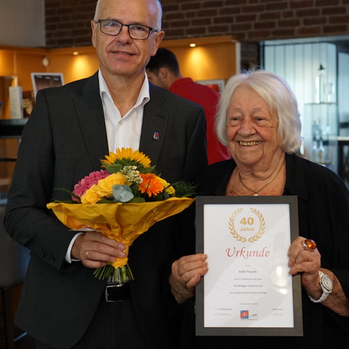Mann mit Brille hält einen Blumenstrauß, neben ihm steht eine lächelnde ältere Frau mit einer Urkunde über 40 Jahre Mitgliedschaft.
