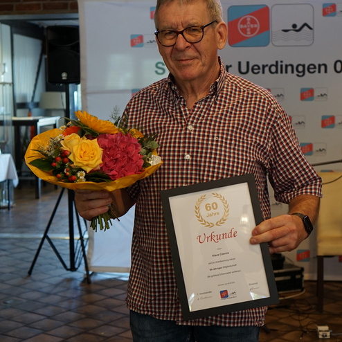 Mann mit Brille hält einen Blumenstrauß und eine Urkunde für 60 Jahre Mitgliedschaft in einem Verein.