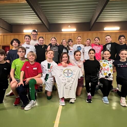 Gruppenfoto von Kindern und Jugendlichen in Sportkleidung, die zusammen auf einer Sportfläche stehen und lächeln.