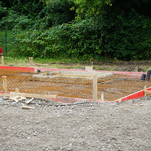 Baugrundst&uuml;ck mit einer vorbereiteten Fundamentplatte, umgeben von Bewehrungsstahl und Holzformwork.