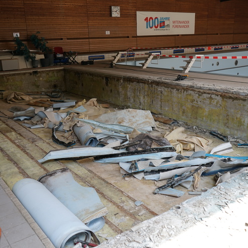 Blick auf einen leeren Schwimmbecken mit herumliegenden Abf&auml;llen und Renovierungs-Materialien in einem Sportzentrum.