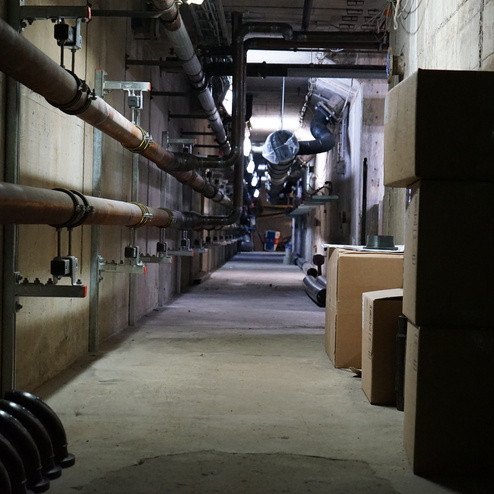 Dunkler Flur mit Metallrohren an der Wand und Kartons, die am Boden gestapelt sind.