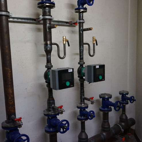 Rohrleitungsanlage mit zwei Pumpensteuerungen, Ventilen und verschiedenen Verbindungselementen an einer Wand.