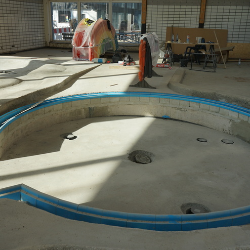 Bau eines Pools mit blauer Fliesenumrandung in einem hellen Raum mit Baustellenmaterial.