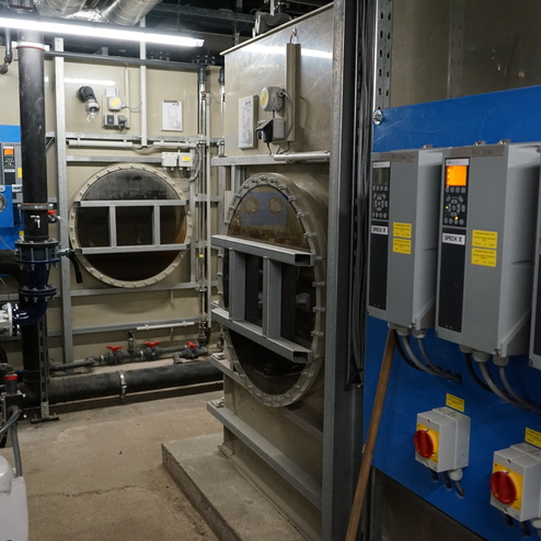 Technikraum mit gro&szlig;en runden Beh&auml;ltern, Rohren und Steuerger&auml;ten an einer blauen Wand.