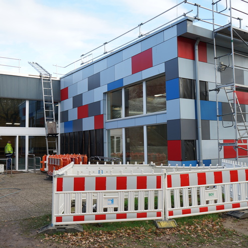 Baustelle mit einem modernen Geb&auml;ude, farbige Fassadenplatten, Bauger&uuml;st und Absperrung im Vordergrund.