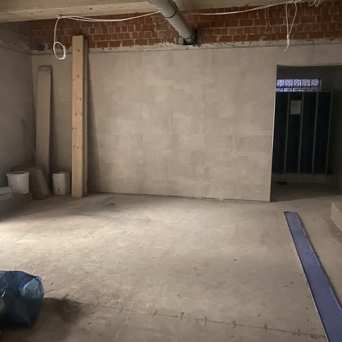 Leere Baustelle mit ungepflastertem Boden, einer Wand aus Fliesen und Werkzeugen in der Ecke.