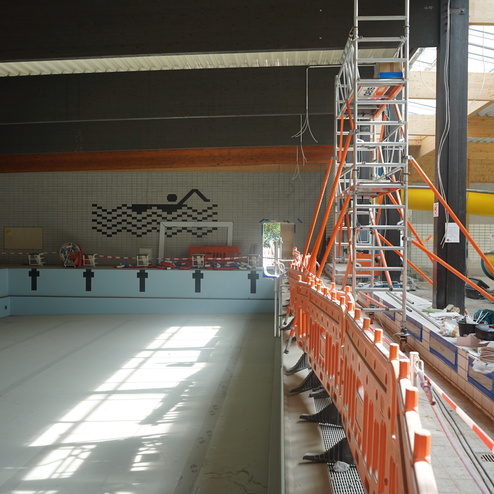 Blick auf ein leerstehendes Schwimmbecken mit Baumaschinen und einer Rutsche im Umbaustadium eines Hallenbades.