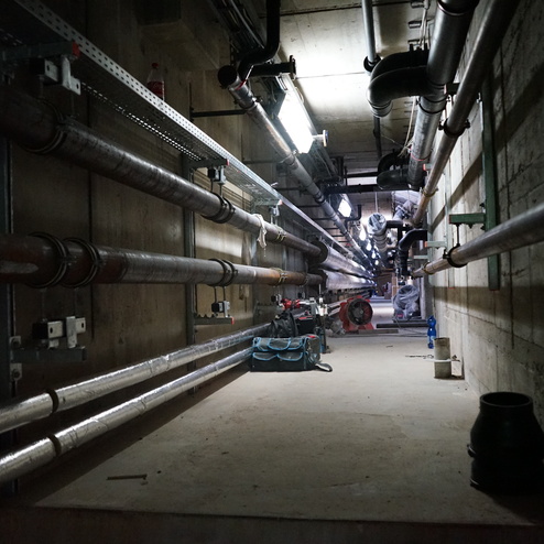 Dunkler Gang mit mehreren Rohren an den W&auml;nden und einer Baustellenausr&uuml;stung auf dem Boden.