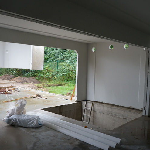 Blick in einen Bauraum mit unvollendeter Wand, Leiter, Bauzubeh&ouml;r und ge&ouml;ffnetem Fenster zur Au&szlig;enansicht.