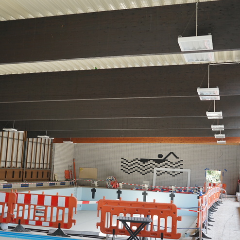 Innenansicht eines Schwimmbads mit Baustellenabsperrung und schwimmendem Wandbild eines Schwimmers auf einer Ziegelwand.