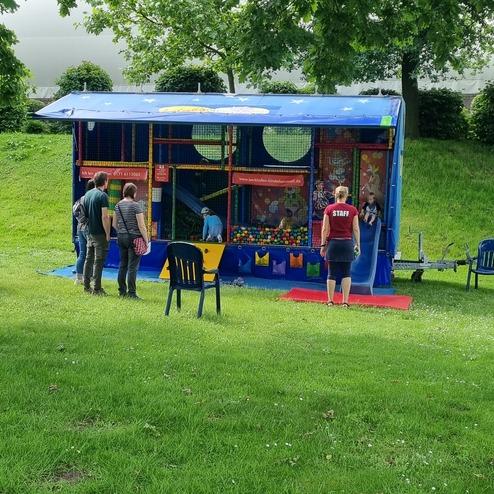Bunte Spielstation mit Kindern und Betreuern auf einer Wiese, umgeben von Bäumen und Rasenflächen.