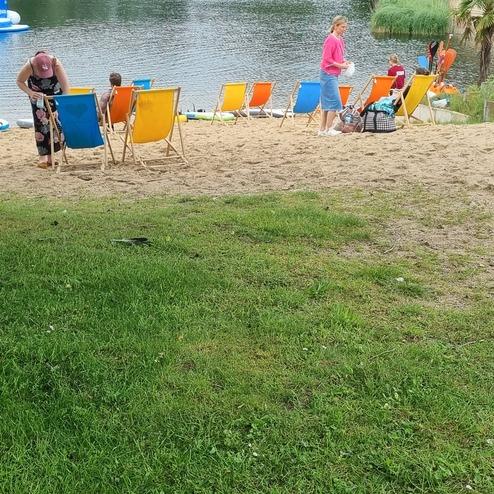 Strandbereich mit mehreren Liegestühlen am Wasser, während zwei Personen am Strand aktiv sind.