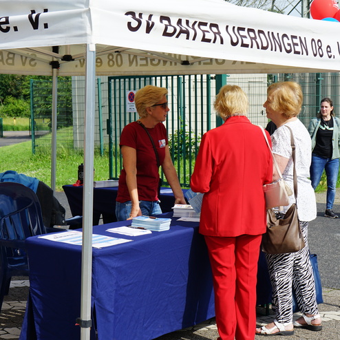 Zelt mit Stand des SV Bayer Uerdingen, drei Frauen unterhalten sich, Informationsmaterial auf Tisch.