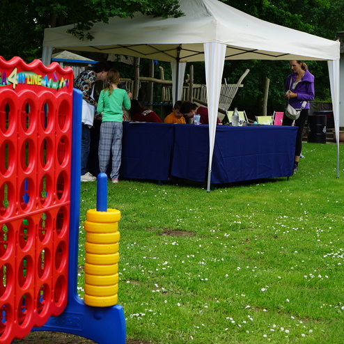 Rot-blaues Mega 4 in Reihe-Spiel auf einer Wiese, im Hintergrund ein Zelt mit Personen, die an einem Tisch stehen.