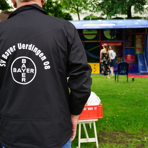 Rückansicht einer Person in einer Jacke mit dem Aufdruck „SV Bayer Uerdingen 08“ vor einem Spielstand.