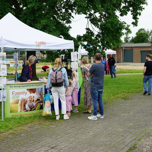 Menschen stehen an einem Informationsstand unter einem Zelt, um Aktivitäten für Familien zu erkunden.