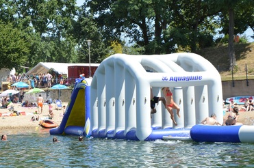 Bunte Beach-Szene mit zahlreichen Menschen, einem aufblasbaren Wasserspielgerät und Sonnenschirmen am Ufer.
